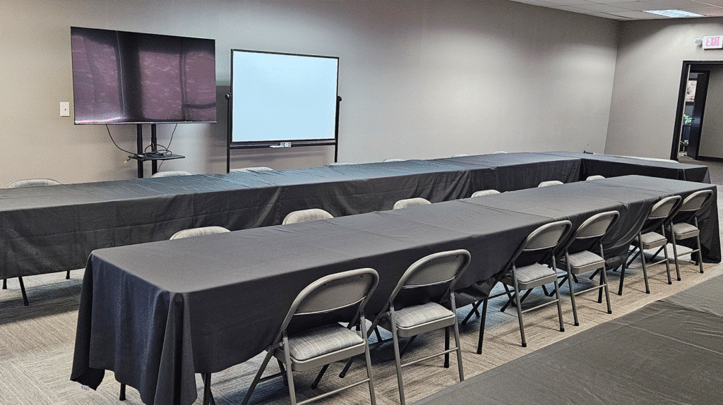 Training room setup with black table covers gray folding chairs wall mounted TV and whiteboard
