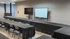 Classroom style training room with black covered tables chairs TV screen and whiteboard