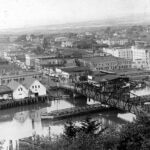 Vintage black and white photo of a large lumber mill or sawmill along the Hoquiam waterfront, with logs floating in the water and workers processing timber.