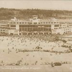 Sepia-toned historic photo of the Seattle-Tacoma International Airport (SEA) terminal with a massive crowd of people gathered outside, symbolizing the airport's central role in creating the SeaTac workforce.