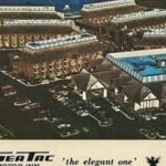 Colored vintage aerial photo showing a large SeaTac-area motel complex with parking lots and multiple brick buildings, illustrating the city's early development as a hospitality and hotel hub near the airport.