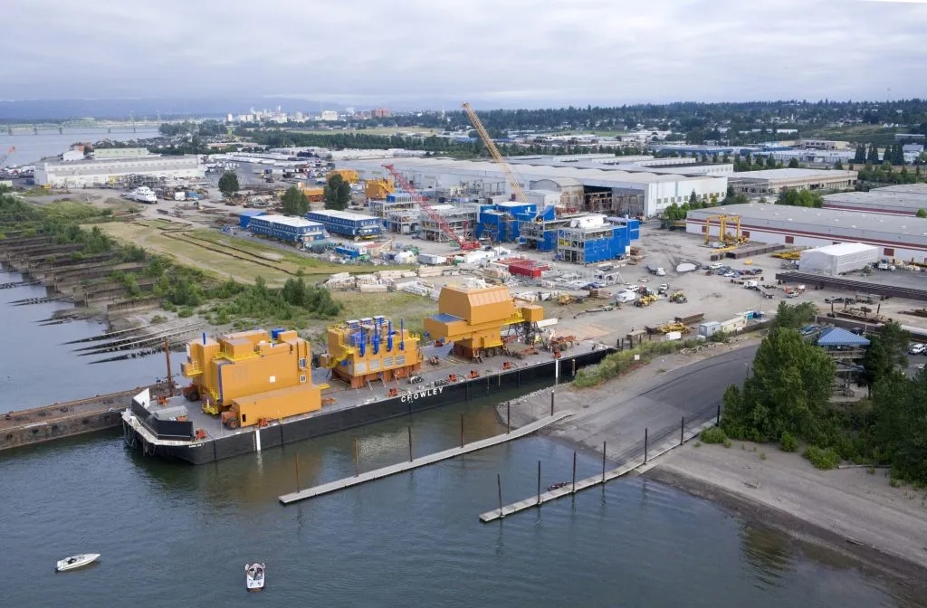 Aerial view of heavy industrial manufacturing and barge logistics at the Port of Vancouver, WA, featuring modular construction along the Columbia River.